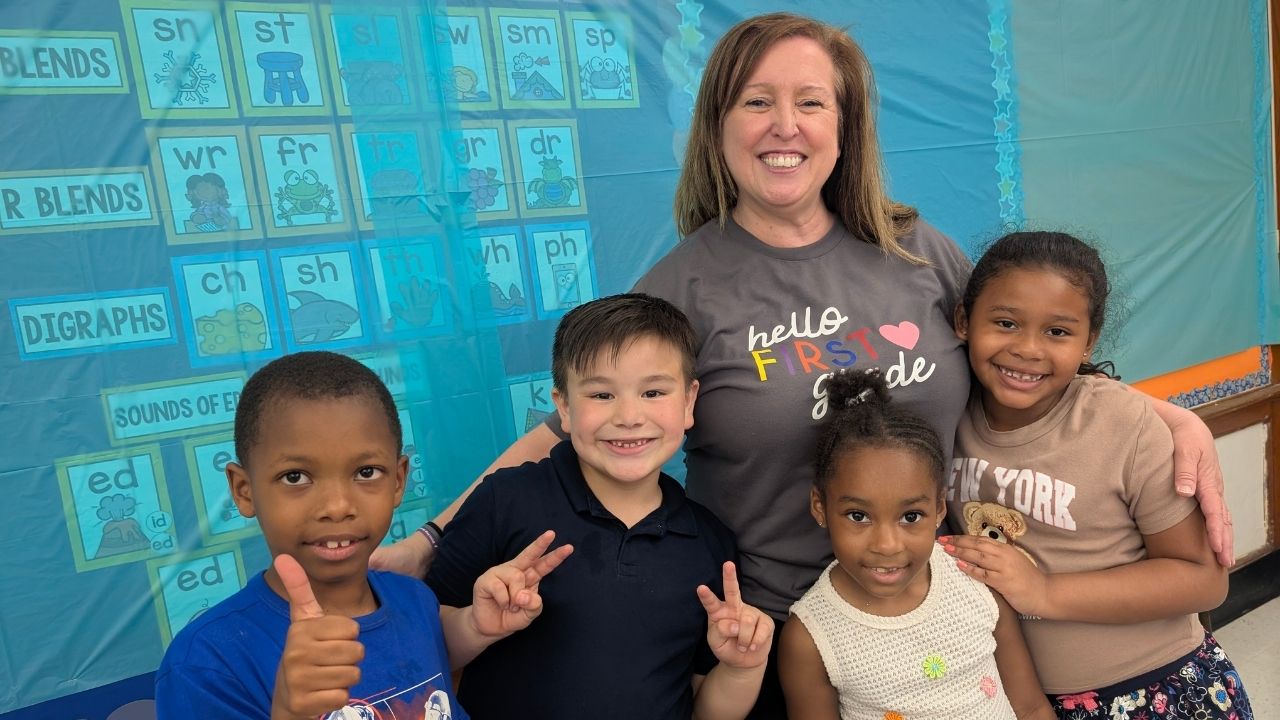 A smiling teacher wearing a grey shirt that says 