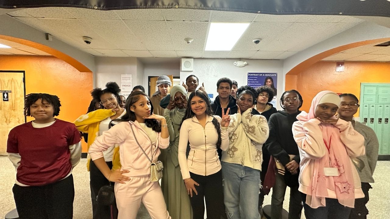 A group of students posing together indoors beneath a overhead banner that reads 