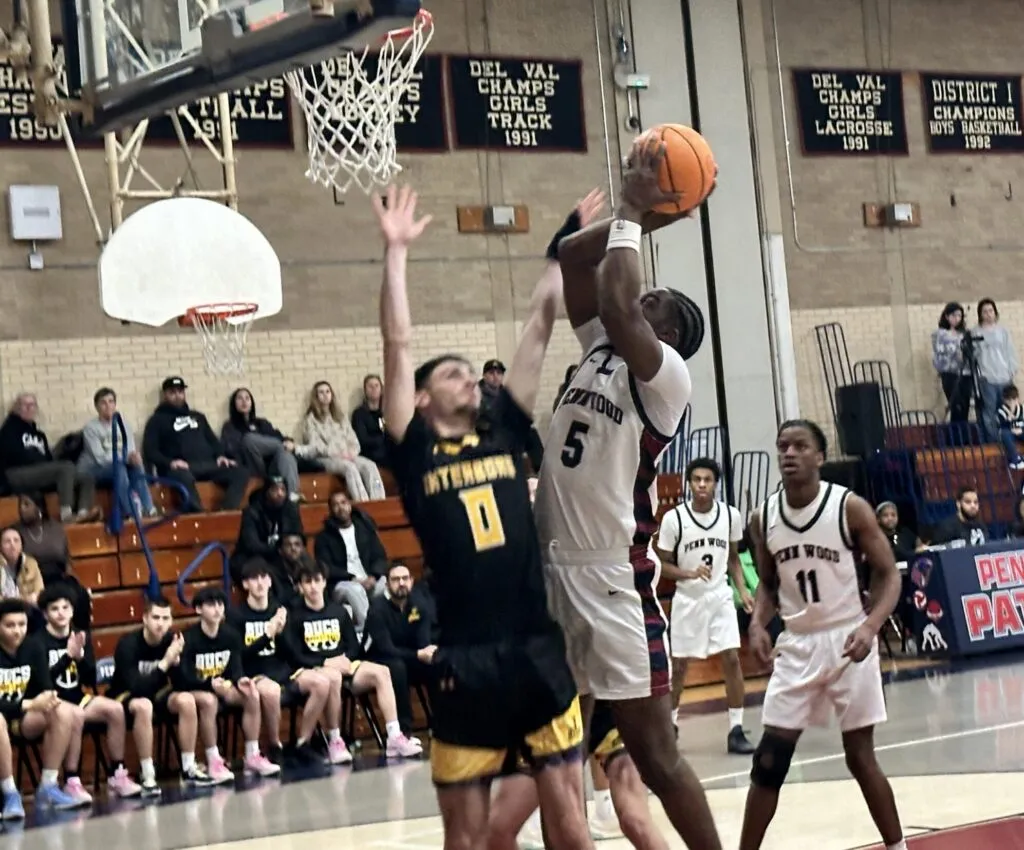 Penn Wood basketball player #5 drives to the hoop for a layup while being defended by an Interboro player. The shot is taken from a low angle near the baseline, showing the hoop and a 