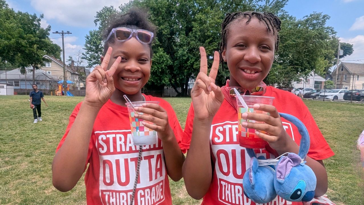 2 students holding cups showing peace signs with their fingers.