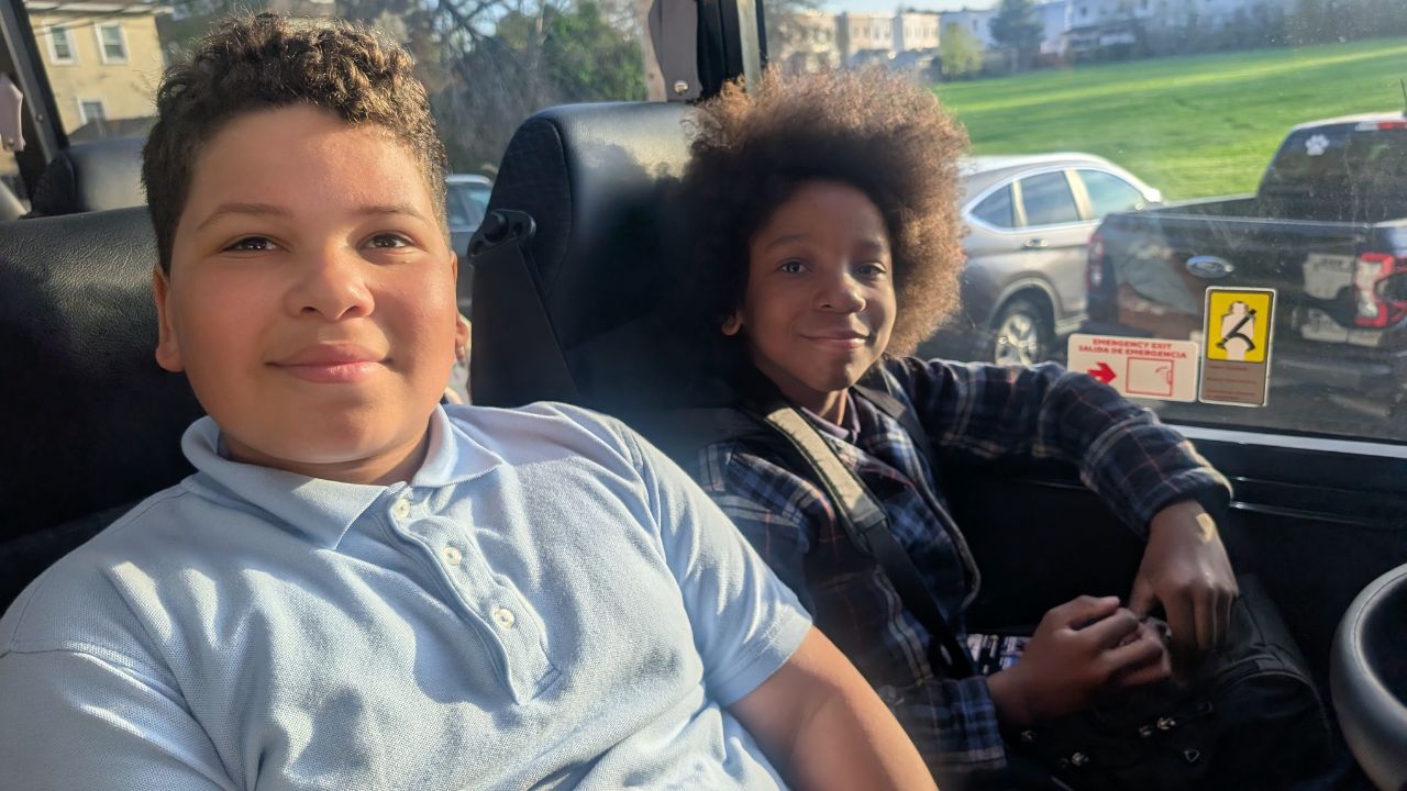 2 students smiling sitting on the bus.