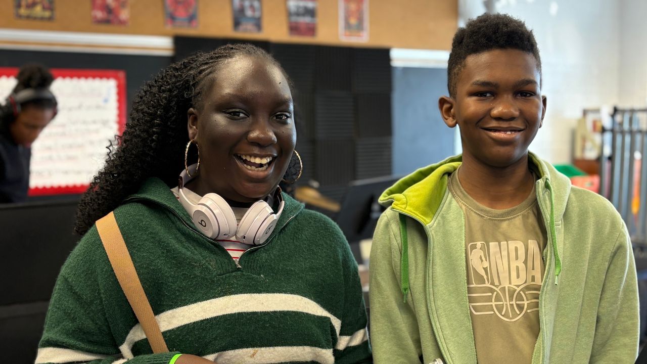 2 students smiling. One wearing white headphones.