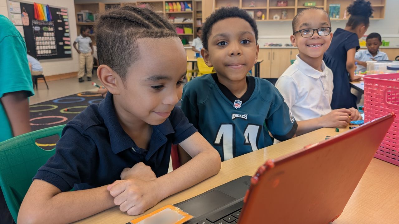 3 young students smiling. One of them looking at a laptop screen.