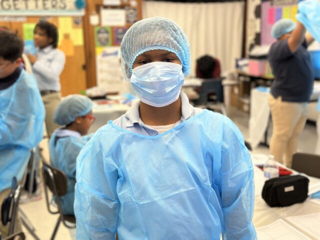 Student wearing hospital scrubs, mask, and head cover. 