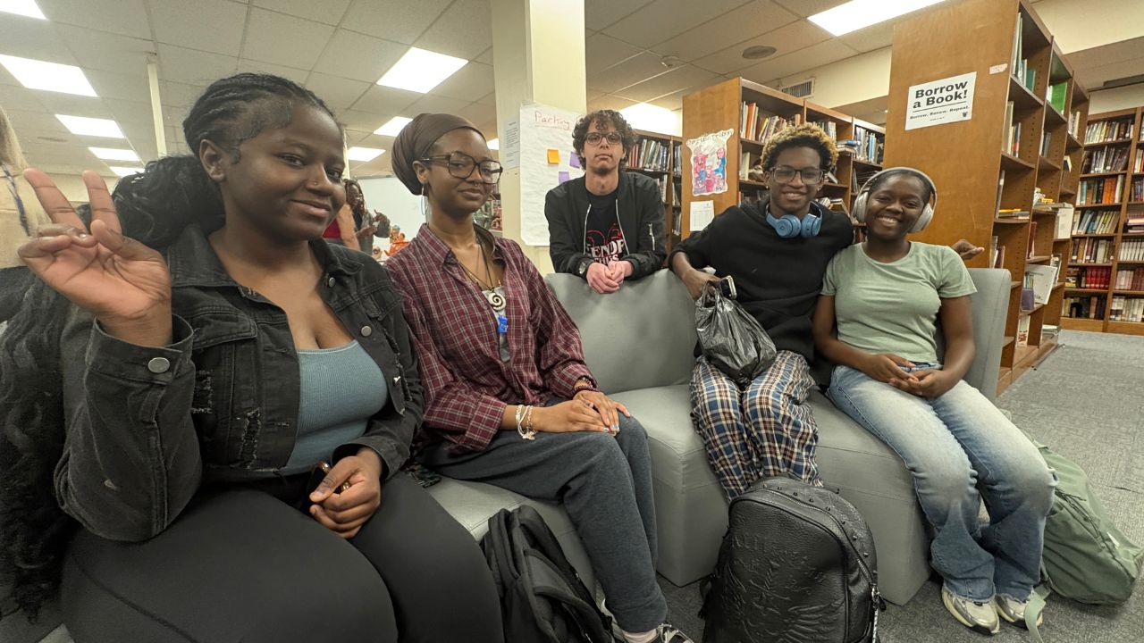 Photo of five smiling students sitting in a library.
