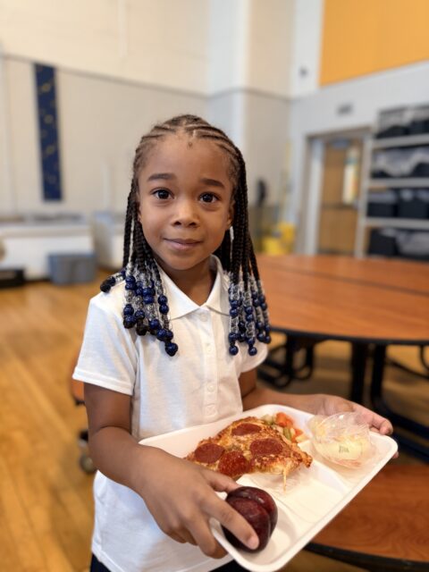 Smiling young student holding a lunch tray with food on it. 